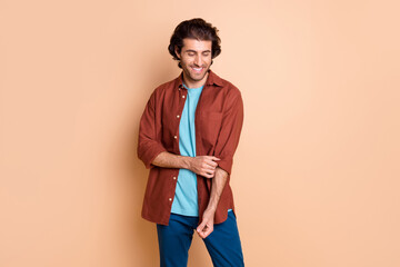 Photo of beaming handsome young guy dressed casual brown clothes fixing shirt sleeve isolated beige color background