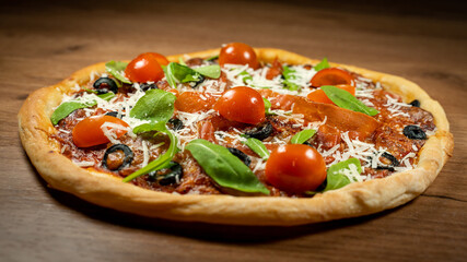 Classic Italian pizza topped with prosciutto, black olives, arugula and cherry tomatoes on rustic wooden surface. Close-up image