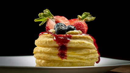 Vol-au-vent puff pastry decorated with fresh strawberries, blueberries and dripping berry coulis on white plate. Close-up image isolated on black background