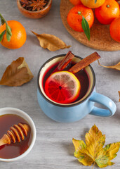 A cup of hot drink with cinnamon, lemon, honey, fruit, spices,  autumn leaves on a table 