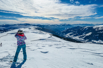Fototapeta na wymiar A woman standing on the snow on top of Katschberg in Austria. She is happy and joyful. Panoramic view on the surrounding mountains. Winter wonderland. Bright and sunny winter day. Love and happiness