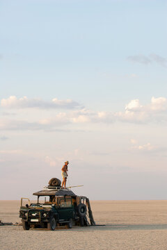 Man standing on top of 4x4 parked on the Makadikadi Salt Pans in Botswana.