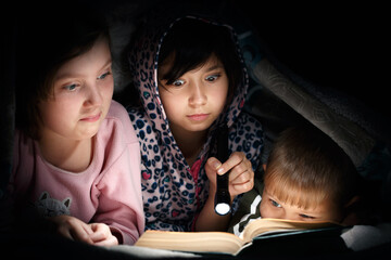 Children reading book under the covers