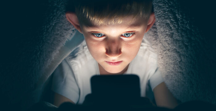 Boy looks at smartphone at night under the covers.