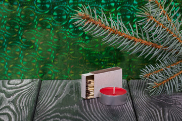 Branches of blue spruce on brushed pine boards. Nearby is a candle and a box of matches. The...