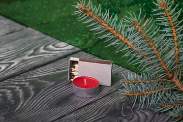 Branches of blue spruce on brushed pine boards. Nearby is a candle and a box of matches. The...