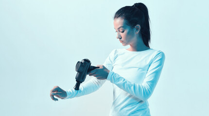 Athletic young female massaging hand by handheld massage gun in neon light, post-workout recovery...