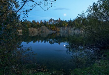 Fototapeta na wymiar Flooded old quarry in the autumn evening. Moon reflection in water. Czech Republic. Europe. 