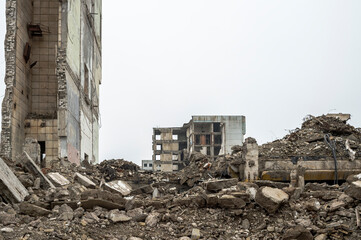A ruined building with a pile of concrete gray debris against a neutral gray sky in a hazy haze....
