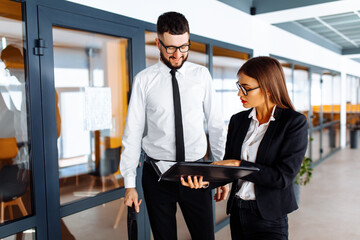 Business colleagues walk along the corridor in the office, discussing documents