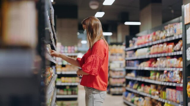 Young woman selecting canned mushrooms showing to her boyfriend consulting searching nutrition together doubting to buy putting back on shelves. Supermarket shopping.