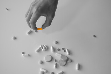 the hand that takes one colorful medicine among the black and white colored drugs. black and white photo with partial coloring.