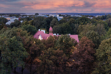 Fototapeta premium Old building surrounded by green park. Evening top view of night Tallinn, Estonia. Dramatic sunset sky