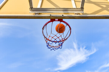 A basketball ball flies into a hoop with a net against a blue cloudy sky. Sports activities on the...