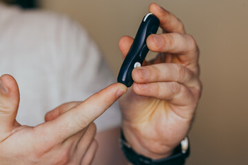 Close up of a man's hand using a lancet on his finger to check blood sugar using a glucose meter, using as medicine, diabetes, glycemia, healthcare and people concept.