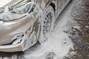 Headlight and wheel of a passenger car in shampoo foam, car wash service, vehicle care