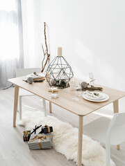 Sunlit room with table decorated for Christmas  dinner with candles, baubles and gift boxes on the floor. Minimalist eco friendly Christmas. Hygge home, simple living concept.