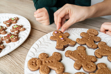 Horizontal detail of unrecognizable mom teaching her kids to make Christmas cookies at home. Ginger Christmas decoration cookies with kids indoors. Seasonal Christmas lifestyle at home with children.