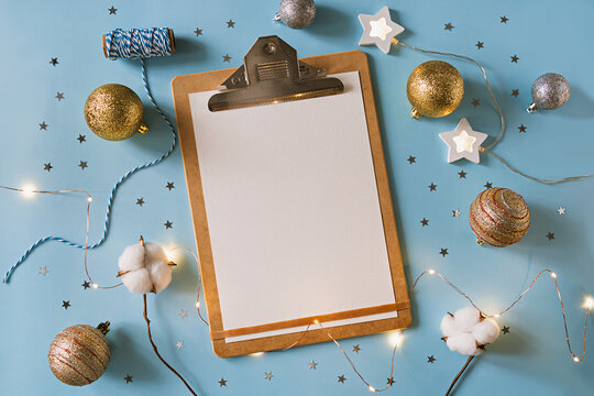 Christmas festive decorations and Paper on clipboard . Wish list and 2021 goals concept. Clipboard mock up, gift, and coton branch with shiny golden balls.New year flat lay, top view, copy space.