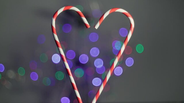 Christmas candy sticks placed in a heart shape with colorful lights out of focus in the background. fleares background. love at christmas.
