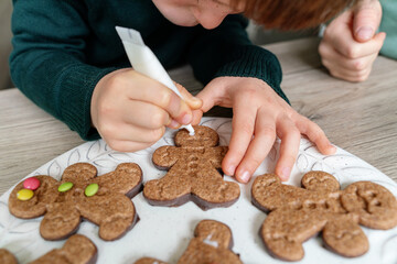 Horizontal detail of unrecognizable children decorating ginger cookies in the kitchen. Christmas recipe of traditional sweet chocolate desserts for the festivities. Lifestyle with kids at home.