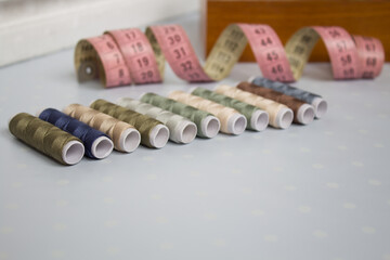 Composition for sewing and tailoring, home sewing, set of various colored firing threads on a light blue background with white dots, there is also a background measuring tape and a wooden box.