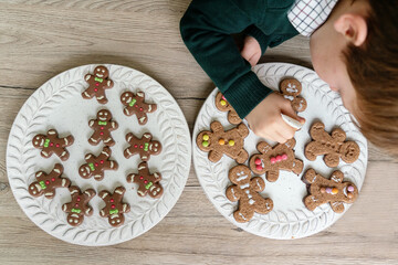 Horizontal view of unrecognizable little kid at home making ginger cookies with chocolate to decorate. Christmas recipe of traditional desserts for the festivities. Lifestyle with kids in the kitchen.