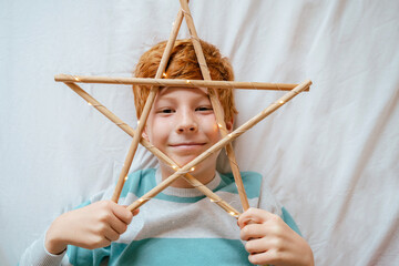 Horizontal top view of little caucasian kid smiling on the bed on Christmas morning. Teen boy holding a Christmas ornament star isolated on white background laughing and smiling at home.