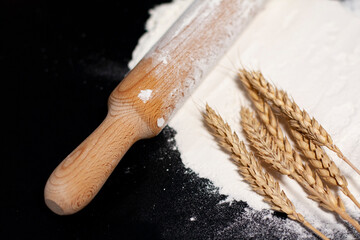 Kitchen wooden roller pin and spikelets of wheat lying on the scattered white flour.