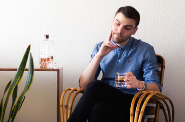 Hombre adulto caucásico y apuesto disfrutando de un whisky escocés sentado en un sillón relajado en un ambiente cálido y reconfortante