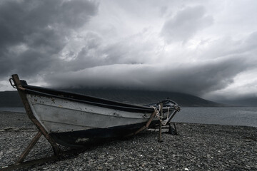 Old row boat and dramatic storm clouds around the peak of Hólmatindur