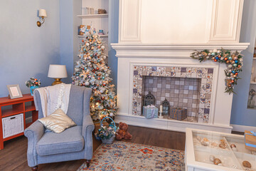 Classic Christmas decorated interior room, New year tree with silver decorations. Modern blue classical style interior design apartment with fireplace and armchair. Christmas eve at home.