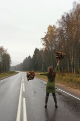 A woman in a green dress with autumn leaves in her hands is walking along the highway