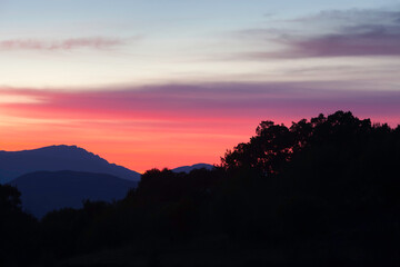 Obraz premium Amazing, vivid colors of a sunset sky and silhouette mountains and trees in the foreground