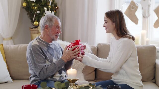 Young woman giving present to happy grandfather indoors at home at Christmas.