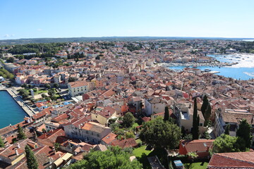 Fototapeta premium Top view of the old town of Rovinj, seaport, houses with red roofs and the sea, Croatia. The tiled roofs of the old city against the background of the bright blue sea and sky, on a sunny autumn day