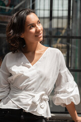 Young Latin brunette woman with short hair, distracted and smiling, wearing a white blouse, photo in the day