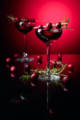 Cranberry liquor with berries and rosemary on a red background.