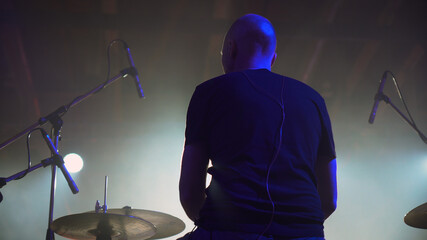 Closeup back view the drummer plays rock on music festival. View from the stage at a European-looking man playing drums, cymbals and percussions.
