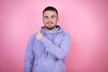 Young handsome man wearing casual sweatshirt over isolated pink background smiling and pointing with hand and finger to the side
