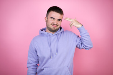 Young handsome man wearing casual sweatshirt over isolated pink background Shooting and killing oneself pointing hand and fingers to head like gun, suicide gesture.