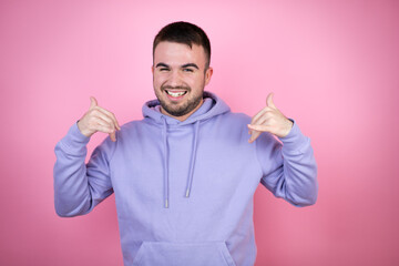 Young handsome man wearing casual sweatshirt over isolated pink background shouting with crazy expression doing rock symbol with hands up