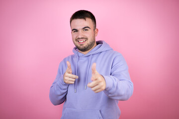 Young handsome man wearing casual sweatshirt over isolated pink background pointing to you and the camera with fingers, smiling positive and cheerful
