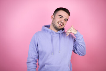 Young handsome man wearing casual sweatshirt over isolated pink background smiling doing phone gesture with hand and fingers like talking on the telephone