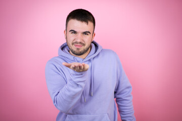 Young handsome man wearing casual sweatshirt over isolated pink background looking at the camera blowing a kiss with hand on air being lovely and sexy. Love expression.