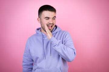 Young handsome man wearing casual sweatshirt over isolated pink background hand on mouth telling secret rumor, whispering malicious talk conversation
