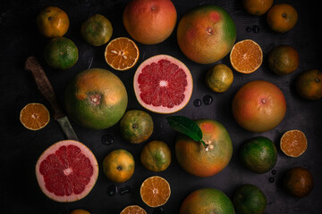 Low key top view of citrus fruits background. Mix of cutted grapefruits and mandarins. Flatlay composition with selective focus