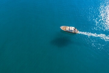 Fototapeta premium Small fishing boat is sailing on the shallow of mediterranean sea at sunny day- Aerial image with copy space