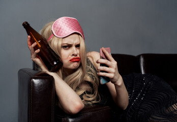 A woman in a pink mask lies on the couch with a bottle of beer and a phone in her hand