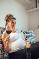 A pregnant woman drinking wine and smoking cigar at home. Unhealthy lifestyle.